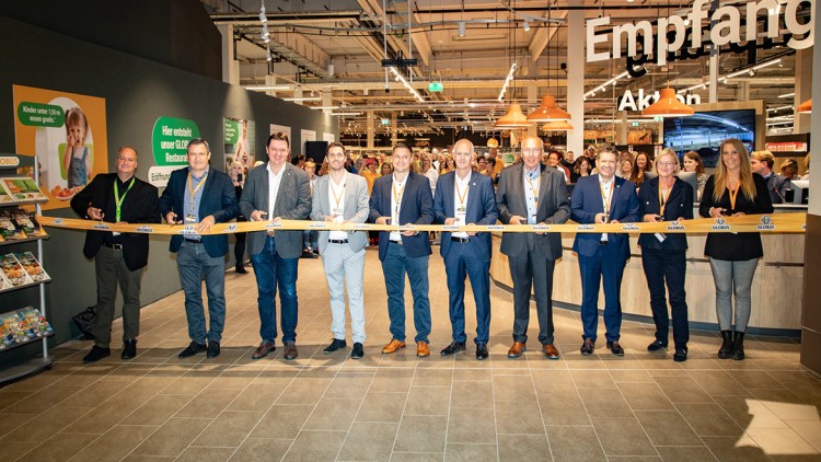 Mehrere Personen schneiden ein gelbes GLOBUS-Band bei einer Eröffnungsfeier in einem hell beleuchteten Markt durch.