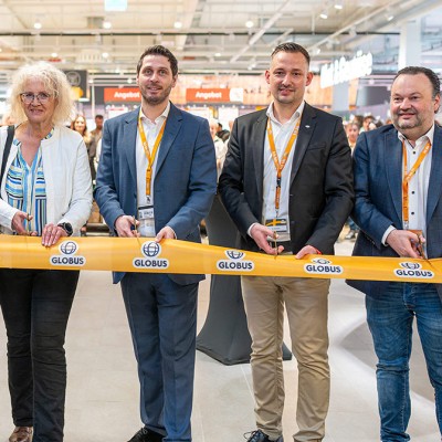 Sechs Personen halten ein gelbes Band mit GLOBUS-Logo in einem hell beleuchteten Einkaufsmarkt.