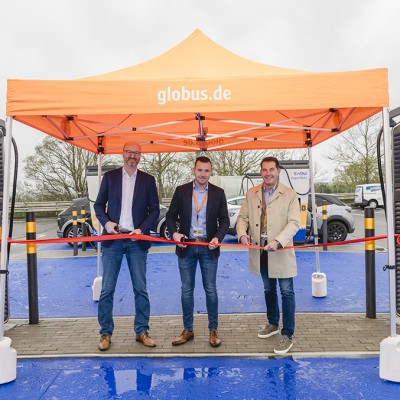 Drei Personen schneiden ein rotes Band unter einem orangefarbenen Pavillon mit der Aufschrift globus.de durch.