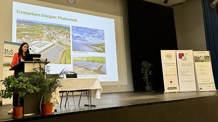 Eine Präsentationsbühne mit Leinwand zeigt Bilder und den Titel „Erneuerbare Energien: Photovoltaik“, daneben Aufsteller mit Logos.