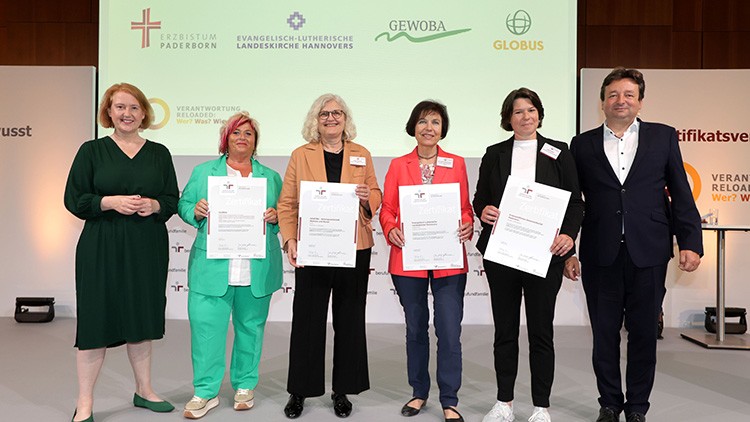 Sechs Personen stehen vor einer Leinwand mit Logos und halten Urkunden in den Händen, darunter das Logo von GLOBUS.