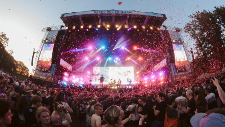 Eine große Menschenmenge vor einer Bühne mit bunten Lichtern, Konfettiregen und dem Schriftzug „ROCCO DEL SCHLACKO“.