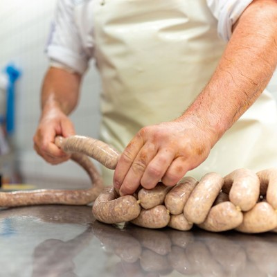 Person formt auf einem Edelstahlarbeitstisch frische Wurst aus einem langen Darm, neben einer silbernen Wurstfüllmaschine.
