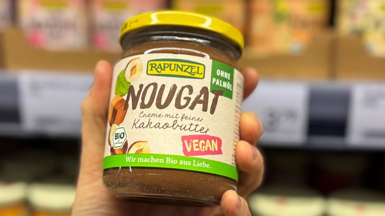 Glas mit veganer Nougatcreme von Rapunzel, Aufschrift: „Ohne Palmöl, Bio, Wir machen Bio aus Liebe“, im Supermarktregal.