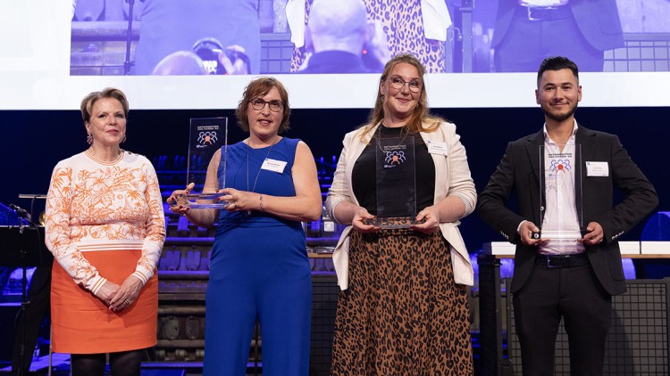 Vier Personen stehen nebeneinander und halten gläserne Auszeichnungen, im Hintergrund eine große Leinwand mit ihrem Bild.