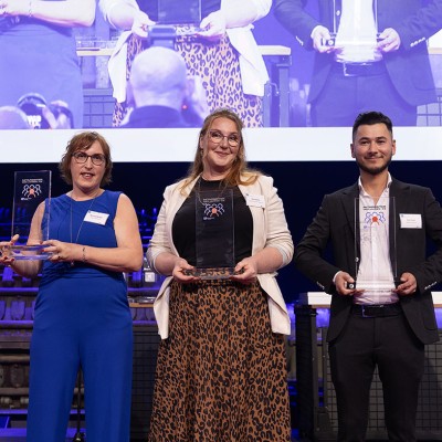 Vier Personen stehen nebeneinander und halten gläserne Auszeichnungen, im Hintergrund eine große Leinwand mit ihrem Bild.