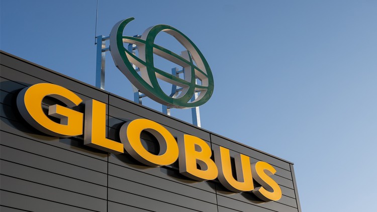 Großes gelbes GLOBUS-Logo auf dunkler Fassade, darüber ein grünes Globus-Symbol vor blauem Himmel.