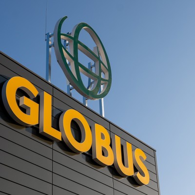 Großes gelbes GLOBUS-Logo auf dunkler Fassade, darüber ein grünes Globus-Symbol vor blauem Himmel.