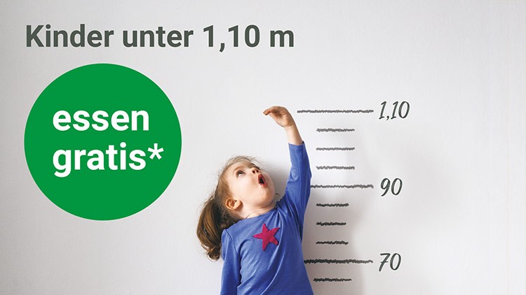 Kind misst seine Größe an einer Skala mit Markierungen bis 1,10 m, daneben steht „Kinder unter 1,10 m essen gratis*“.