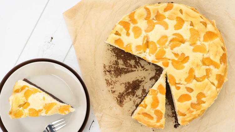 Runder Kuchen mit Mandarinenstücken auf Backpapier, daneben ein Stück auf einem Teller mit Gabel.