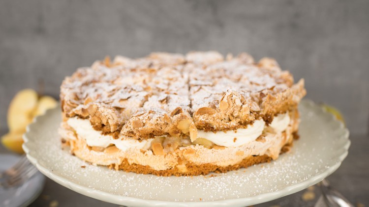 Runde Sahnetorte mit Schichten aus Baiser und Mandeln auf einer Kuchenplatte, bestäubt mit Puderzucker.