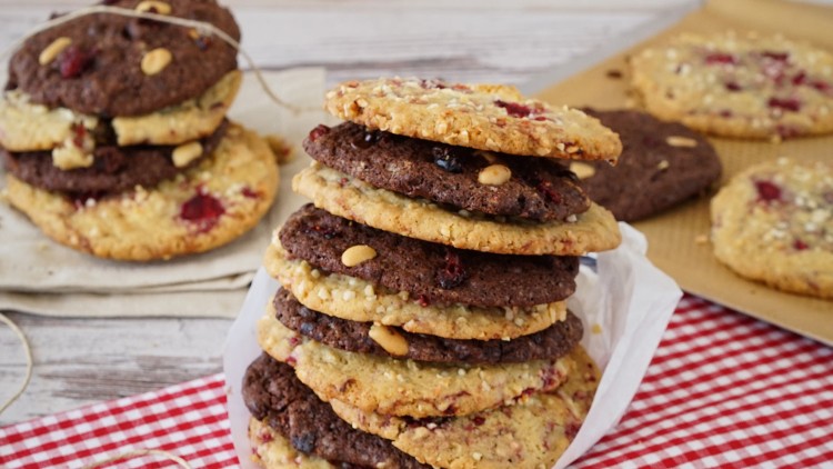 Ein Stapel heller und dunkler Cookies mit Nüssen und getrockneten Früchten liegt auf einem rot-weiß karierten Tuch.