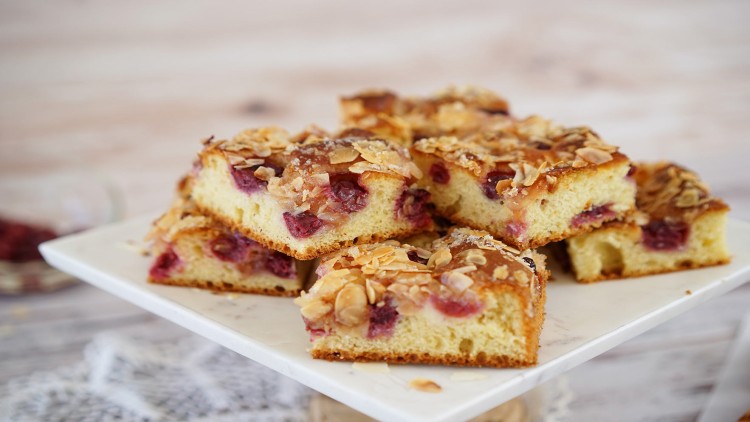 Mehrere Stücke Streuselkuchen mit Kirschen und Mandelblättchen auf einer weißen Kuchenplatte.