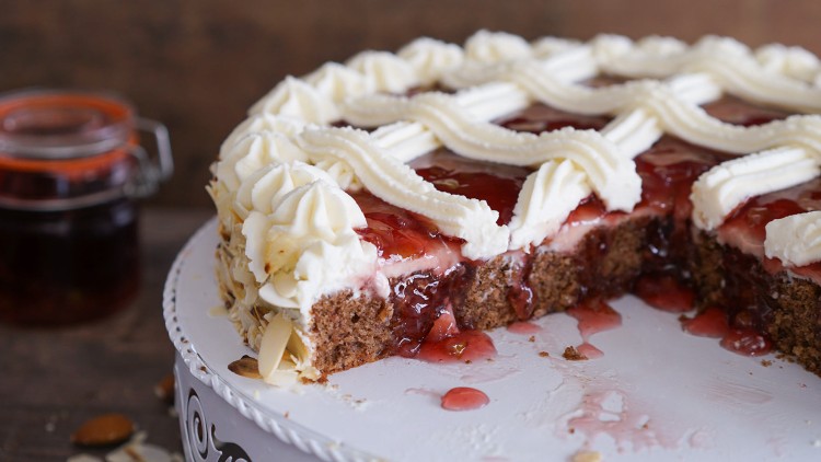 Anschnitt einer Sahnetorte mit roter Fruchtfüllung, Sahnedekor und Mandelsplittern auf einer weißen Tortenplatte.