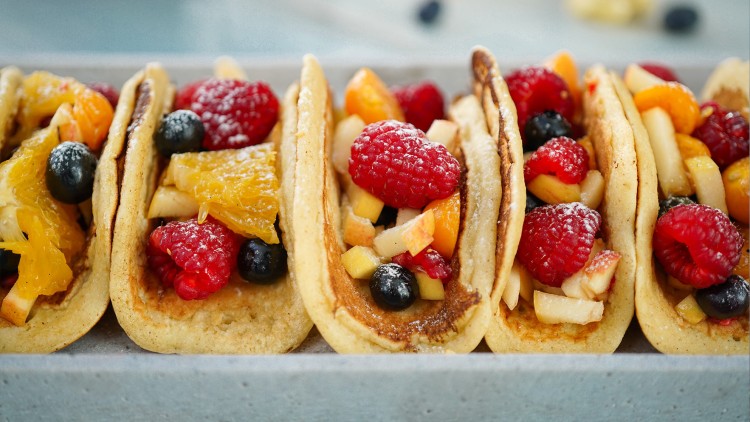 Weiche Pancake-Tacos gefüllt mit frischen Früchten wie Himbeeren, Blaubeeren, Orangenstücken und Apfelschnitzen.