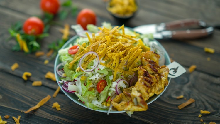 Salatschüssel mit gegrilltem Hähnchen, Streifen aus Tortilla-Chips, Guacamole, Zwiebeln, Tomaten und weiteren frischen Zutaten.