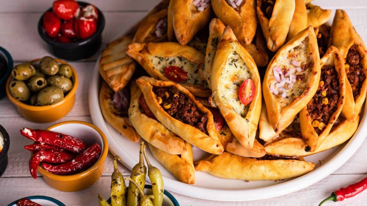 Ein Teller mit gefüllten Teigtaschen, daneben Schalen mit Oliven, gefüllten Paprika, Peperoni und getrockneten Tomaten.