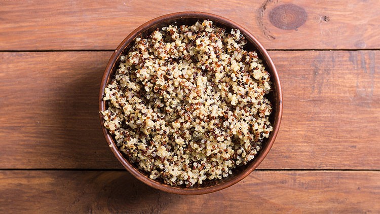 Gekochte Quinoa in einer braunen Schale auf einem Holztisch.