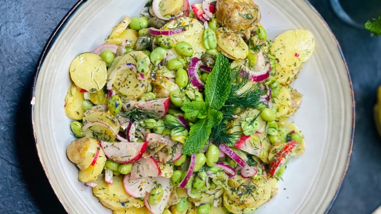 Kartoffelsalat mit Radieschen, Edamame, roten Zwiebeln, frischen Kräutern und Minze auf einem Teller, daneben Zitrone und Minze.