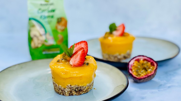 Zwei Desserttörtchen mit gelber Creme, Erdbeere, Minze und Passionsfrucht auf Tellern, grüne Verpackung im Hintergrund.