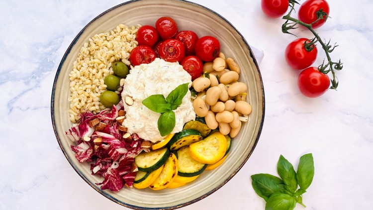 Bunter Salatteller mit Kirschtomaten, Zucchinischeiben, weißen Bohnen, Oliven, Radicchio, Getreide und einer Basilikumgarnitur.
