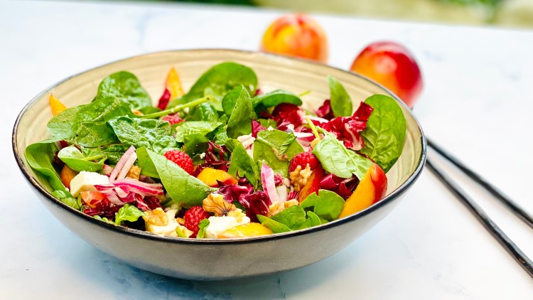 Bunte Schüssel mit frischem Salat aus Blattspinat, Radicchio, Himbeeren, Pfirsichstücken, Zwiebeln, Nüssen und Käsewürfeln.