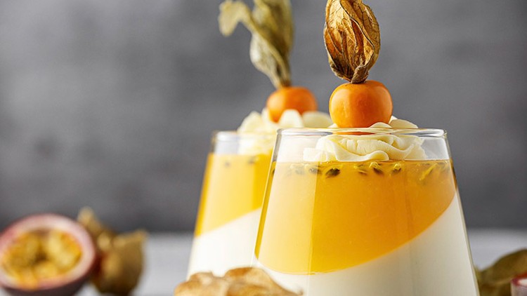 Zwei Gläser mit weißem und gelbem Schichtdessert, dekoriert mit Physalis und Sahnecreme, auf hellem Untergrund.