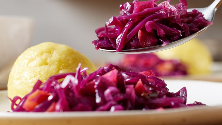 Gelber Kloß und Rotkohl auf einem Teller, ein Löffel hebt Rotkohl hoch.