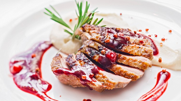 In Scheiben geschnittene Entenbrust mit roter Sauce, Rosmarinzweig und weißem Püree auf einem weißen Teller angerichtet.