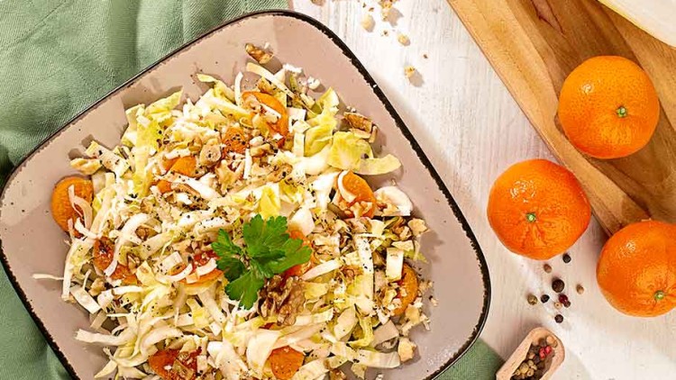 Chicorée- und Mandarinen-Salat mit gehackten Walnüssen auf einem eckigen Teller, umgeben von Zutatendekoration.