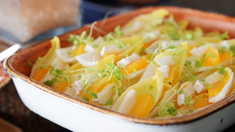 Salat aus Chicorée, Orangenscheiben, weißen Käsewürfeln und frischen Kräutern in einer weißen Auflaufform mit braunem Rand.