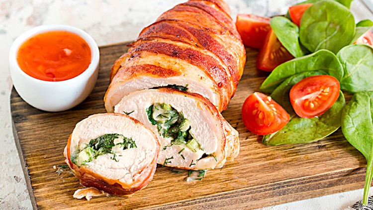 Ein aufgeschnittenes Hähnchenfilet mit Käse-Spinat-Füllung und Bacon, dazu frischer Spinat, Cocktailtomaten und rote Soße.