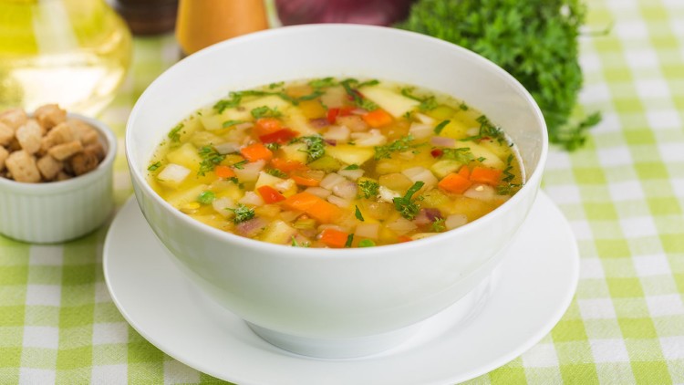 Weiße Schale mit Gemüsesuppe aus Würfeln von Kartoffeln, Karotten und Sellerie, daneben Croutons in einer kleinen Schale.
