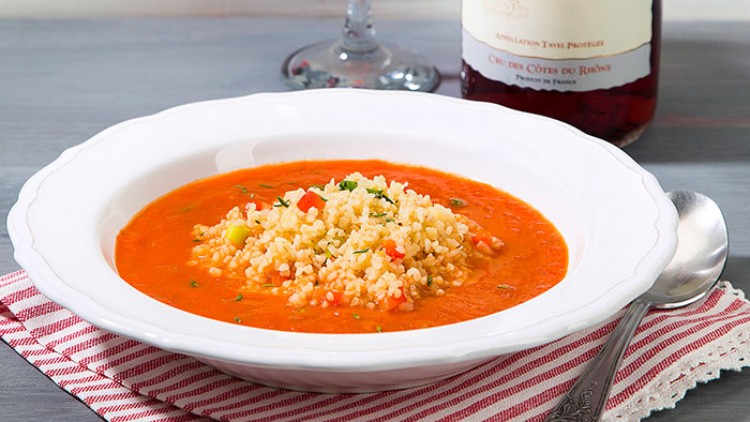 Roter Teller mit Suppe und Bulgur, daneben eine Flasche Rotwein, ein Weinglas und ein Löffel auf einem gestreiften Stofftuch.
