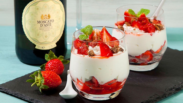 Zwei Gläser mit Erdbeerdessert und Minzdeko auf schwarzem Untergrund, daneben eine Weinflasche „Moscato d’Asti“ und Erdbeeren.