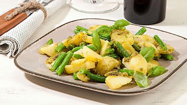 Kartoffelsalat mit grünen Bohnen und frischem Basilikum auf einem Teller, daneben Besteck, ein Weinglas und eine Weinflasche.
