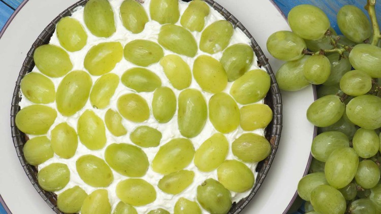 Runde Torte mit einem Belag aus grünen Weintrauben auf weißer Creme, daneben grüne Weintrauben auf einem Teller.