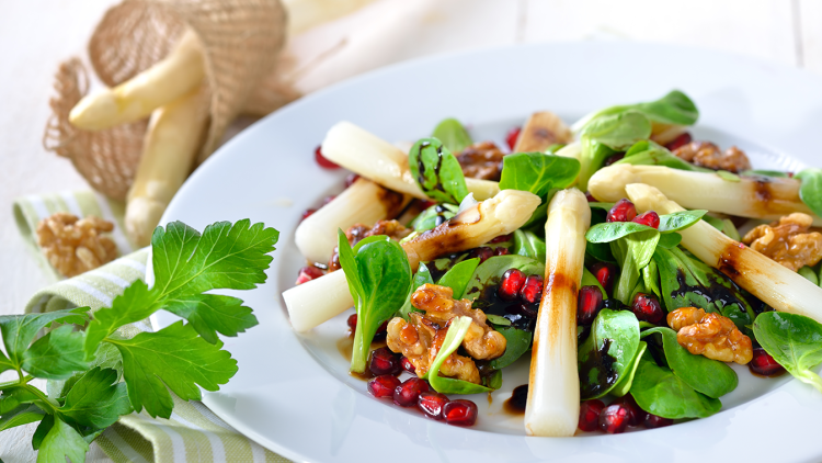 Weißer Spargel mit Feldsalat, Walnüssen, Granatapfelkernen und Balsamico-Dressing auf einem weißen Teller angerichtet.