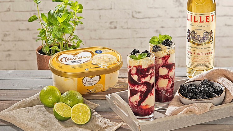 Zwei Gläser mit Dessert, Vanilleeis, Limetten, eine Schale Brombeeren, Lillet-Flasche und Topf mit frischer Minze auf Holztisch.