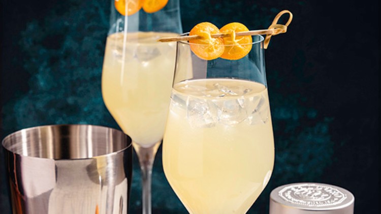 Zwei mit Eis und gelbem Getränk gefüllte Gläser mit Kumquats am Rand, daneben ein Shaker, Kumquats und eine Dose SALDORO Ursalz.