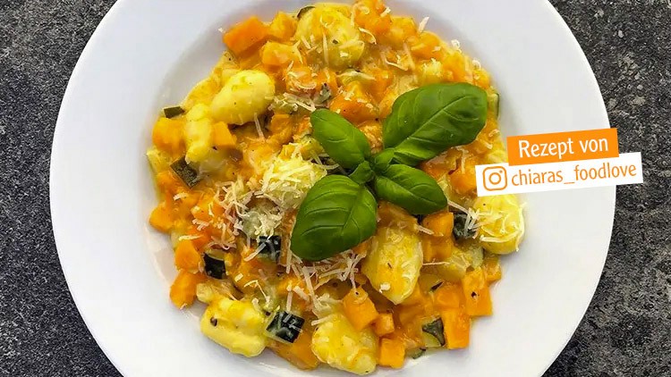 Gnocchi mit Kürbiswürfeln, Zucchini, geriebenem Käse und Basilikum auf weißem Teller, Text: Rezept von @chiaras_foodlove.