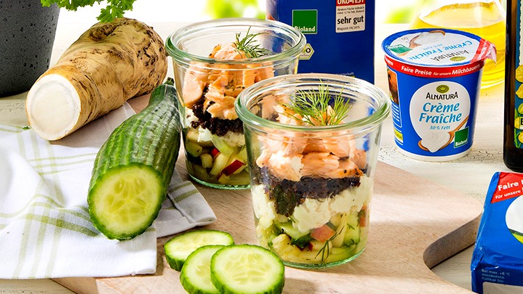 Ein gedeckter Tisch mit Frischkäse, Vollmilch, Süßrahmbutter, Rapsöl, Kräutern, Gurke, Meerrettich und zwei Gläsern Lachsgericht.