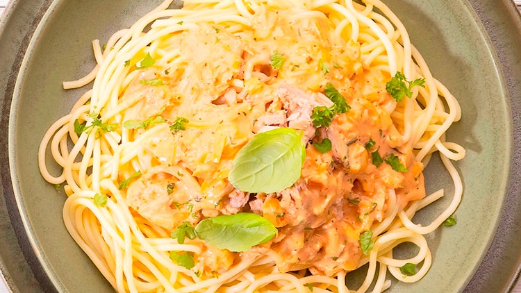 Teller mit Spaghetti, hellroter Sahnesoße, Thunfischstücken und grünen Kräutern, dekoriert mit Basilikumblättern.