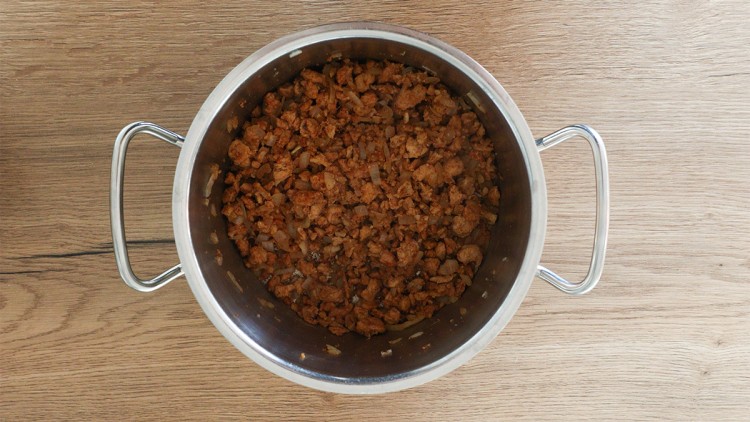 Gekochtes, krümeliges Hackfleisch mit Zwiebelstücken in einem silbernen Topf auf einer Holzoberfläche.
