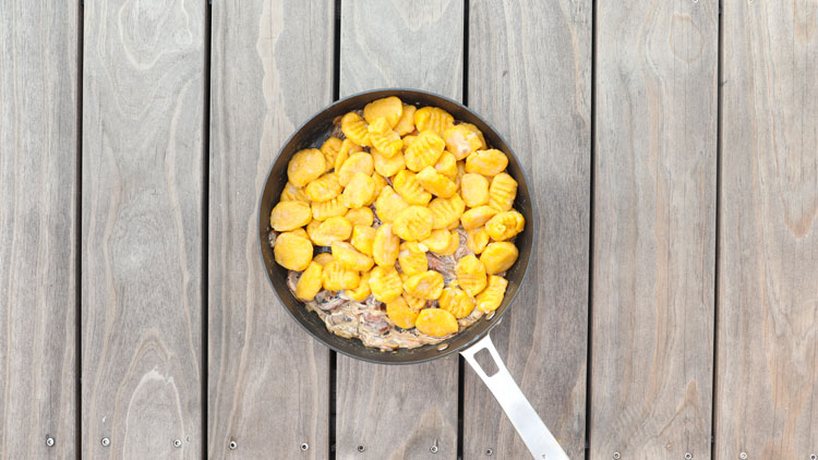 Vollformatige Pfanne mit goldgelben Gnocchi und rahmiger Soße auf einem Holztisch mit hellbraunen Holzplanken.
