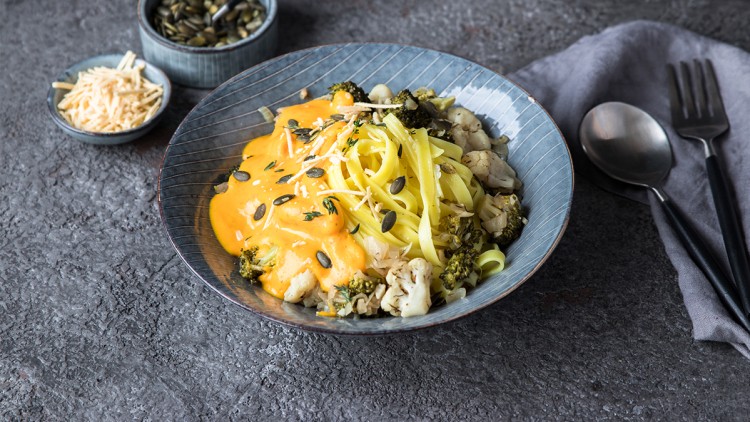 Tagliatelle mit Brokkoli, Blumenkohl, Kürbiskernsoße, Kürbiskernen und geriebenem Käse auf grauem Untergrund.