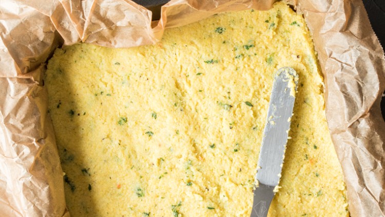 Quiche-Teig mit Kräutern liegt in braunem Backpapier in einer Form, ein silbernes Messer liegt auf dem Teig.