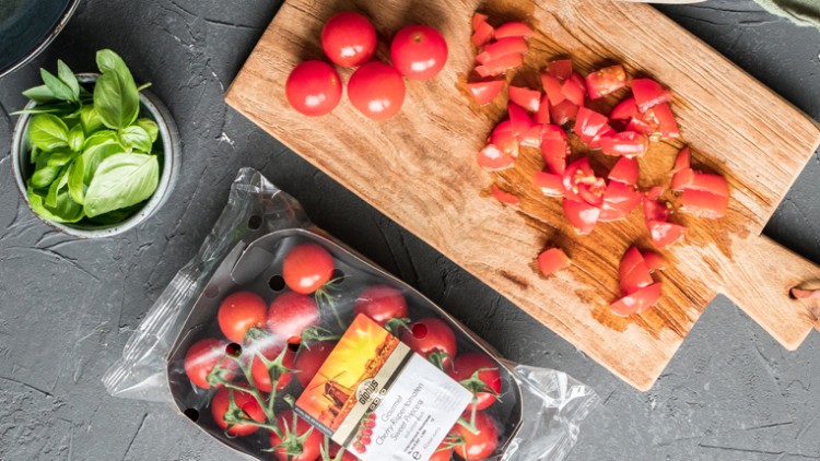 Kirschtomaten in einer Plastikverpackung, gehackte und ganze Tomaten auf Holzbrett sowie frische Basilikumblätter in einer Schale.