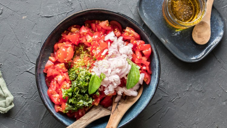Schüssel mit gehackten Tomaten, Zwiebeln, Basilikum und Kräutern, daneben ein Teller mit Olivenöl und Holzlöffeln.