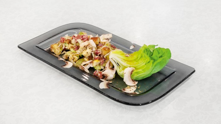 Salat aus grünem Kopfsalat, gebratenen Kartoffelstücken, Pilzen und roten Zutaten auf schwarzem rechteckigem Teller.